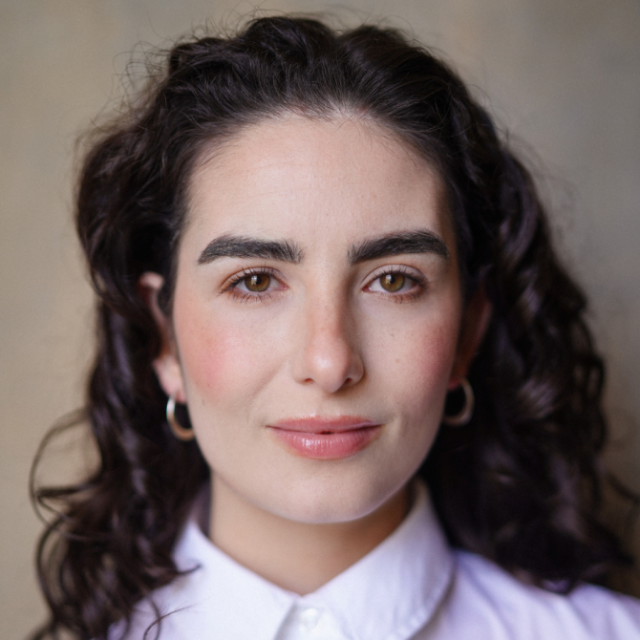 Woman with curly dark hair and hoop earrings, wearing a white shirt, looking directly at the camera