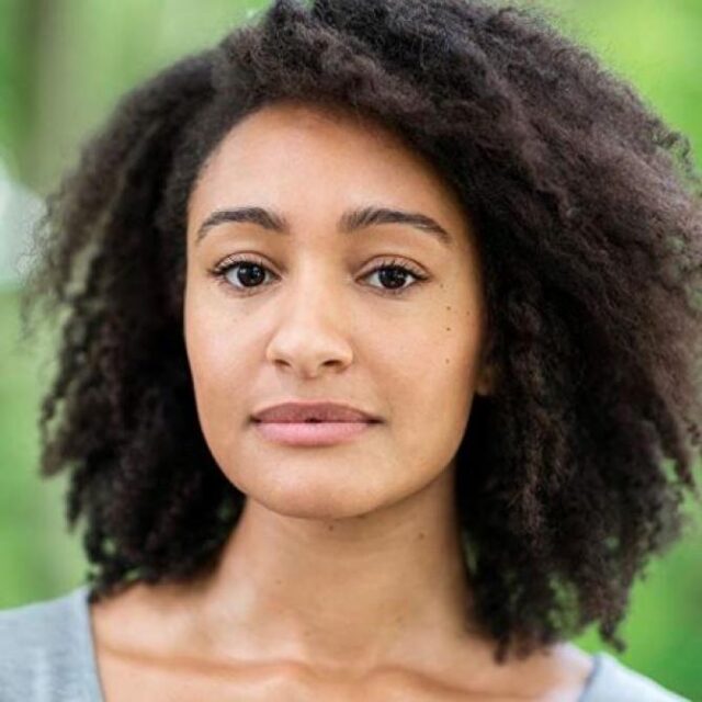 Close-up portrait of a woman with curly hair, looking directly at the camera with a neutral expression