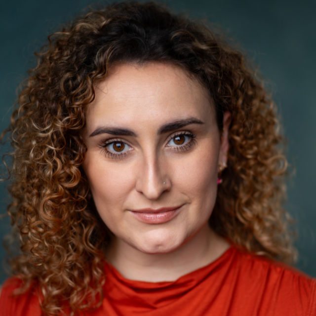 Woman with curly hair wearing an orange top, smiling gently at the camera