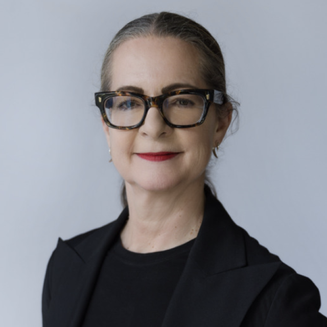 Portrait of a woman with tortoiseshell glasses and red lipstick, wearing a black jacket