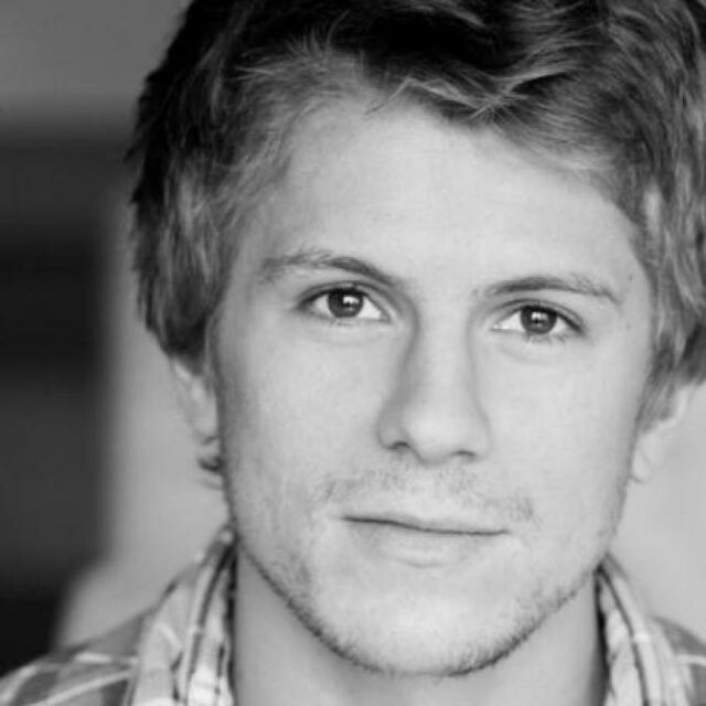 Black and white close-up portrait of a young man with tousled hair, wearing a checked shirt