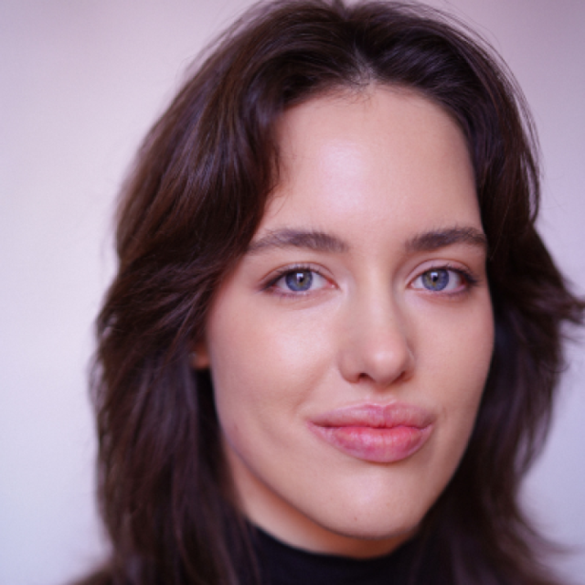 Close-up portrait of a young woman with dark wavy hair, green eyes and a neutral expression, looking directly at the camera
