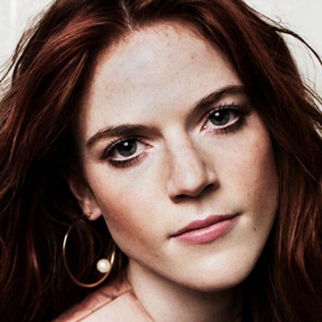 Close-up portrait of a red-haired woman with freckles, wearing a hoop earring, looking directly at the camera