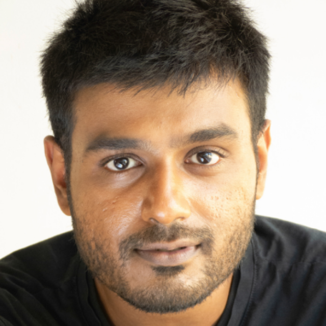 Close-up portrait of a man with short dark hair and stubble, wearing a black top