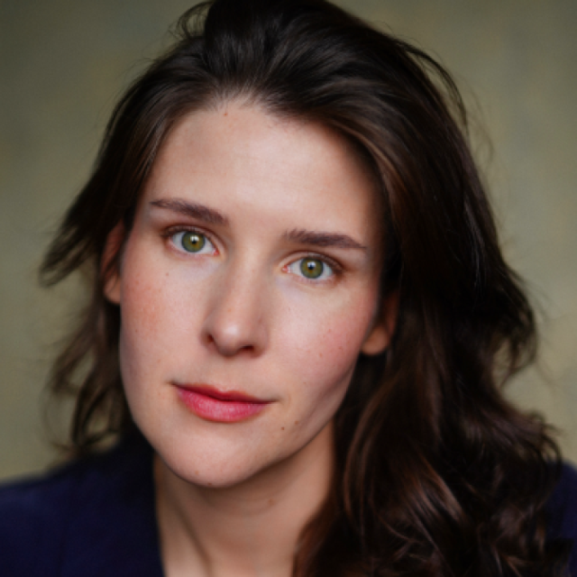 Close-up portrait of a woman with long dark wavy hair and green eyes, looking directly at the camera