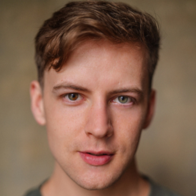 Close-up portrait of a young man with wavy brown hair, looking directly at the camera