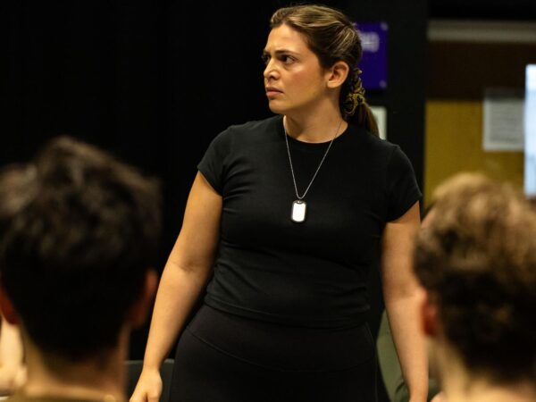 A woman stands addressing a seated group during a rehearsal or workshop session