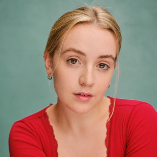 Close-up portrait of a young woman with blonde hair wearing a red top, against a teal background