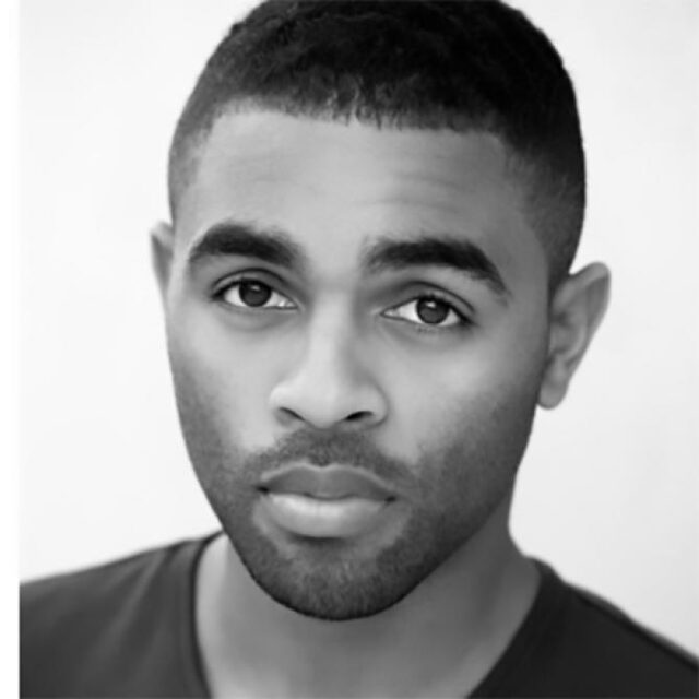 Black-and-white headshot of a man with short hair and a trimmed beard, looking directly at the camera