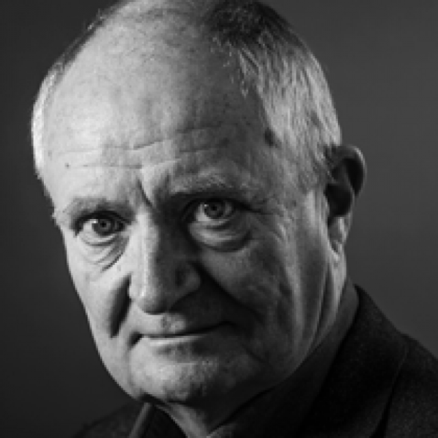 Black-and-white studio portrait of an older man with a serious expression, wearing a dark jacket
