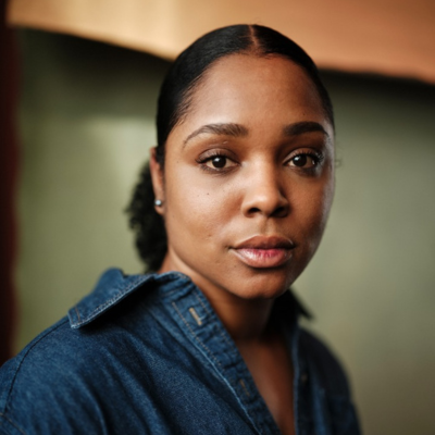 Portrait of a woman with dark hair pulled back, wearing a denim shirt, looking directly at the camera