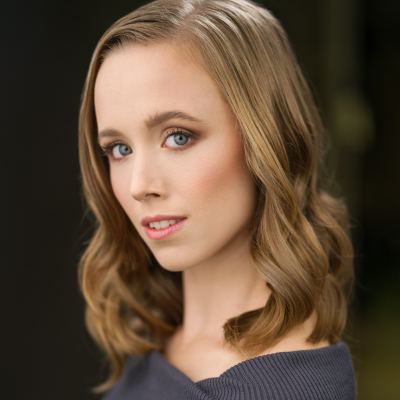 Headshot of a young woman with wavy blonde hair, blue eyes, and an off-the-shoulder grey top
