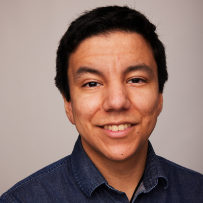 Headshot of a smiling man with short dark hair, wearing a navy denim shirt against a plain background