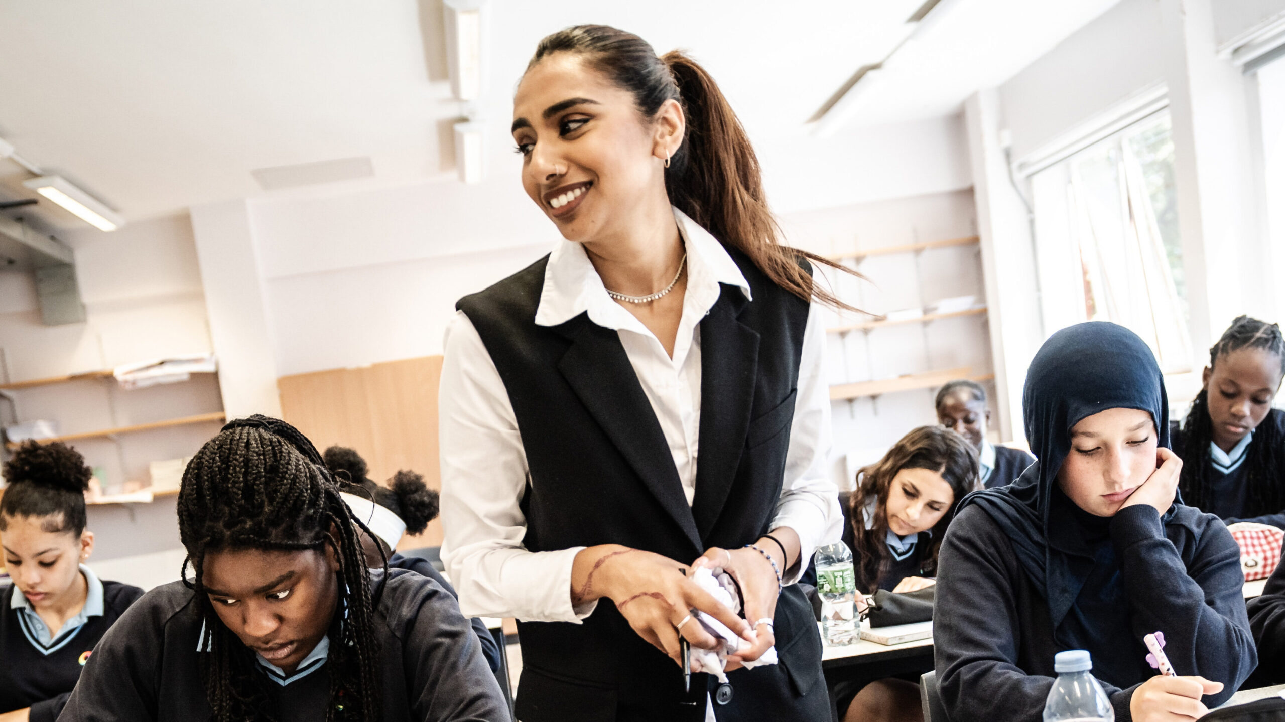 A teacher stands in a classroom with a group of learners working at desks