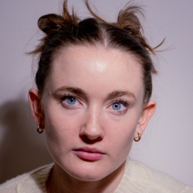 Close-up portrait of a woman with blue eyes, hair styled in two buns, wearing small hoop earrings