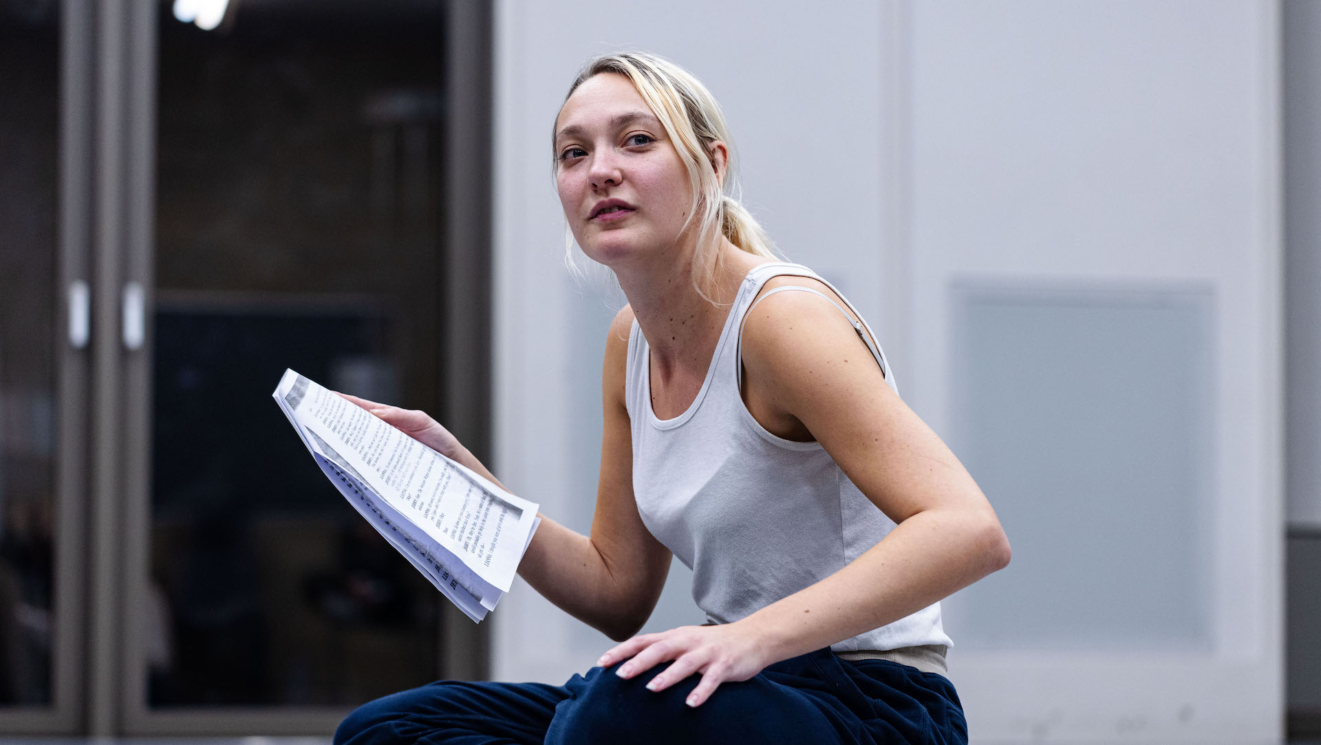 Actress holding script pages during a rehearsal, looking up while seated
