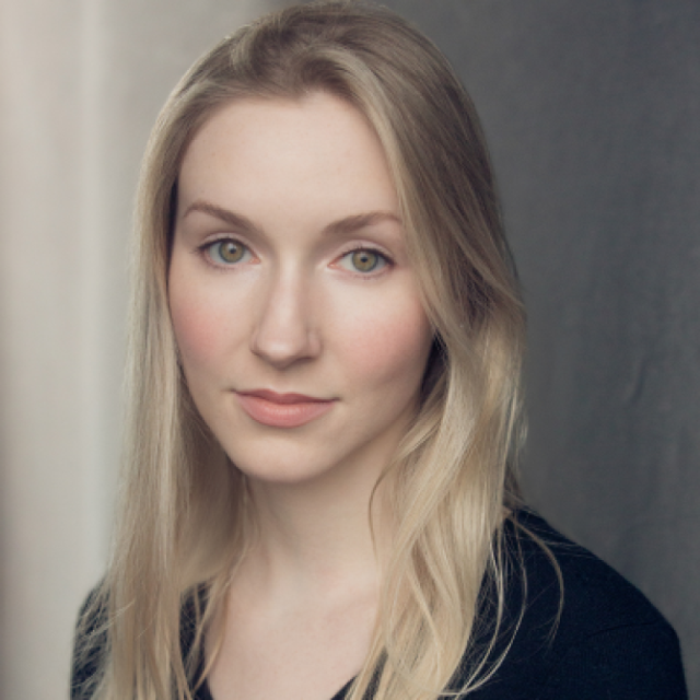 Headshot portrait of a young woman with long blonde hair, wearing a black top, against a grey background