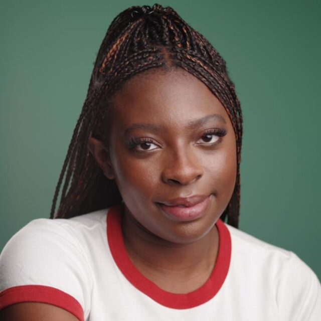 Woman with long braided hair wearing a white top with red trim, smiling against a green background