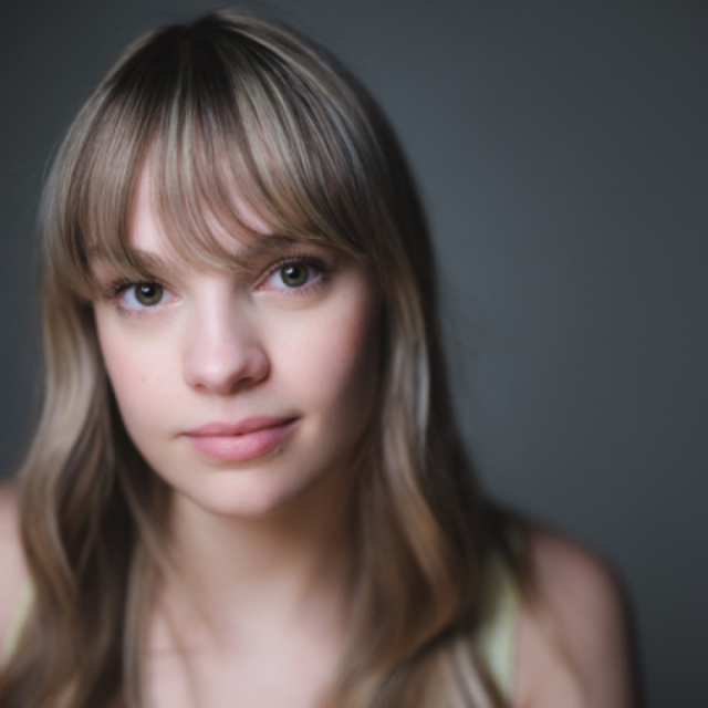 Portrait of a young woman with wavy light brown hair and a fringe, looking at the camera