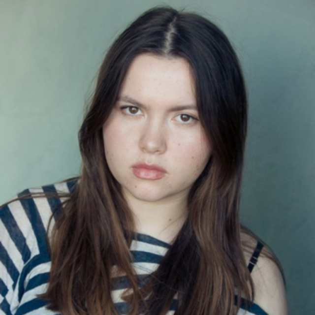 Young woman with long dark hair and a serious expression, wearing a striped top against a plain background