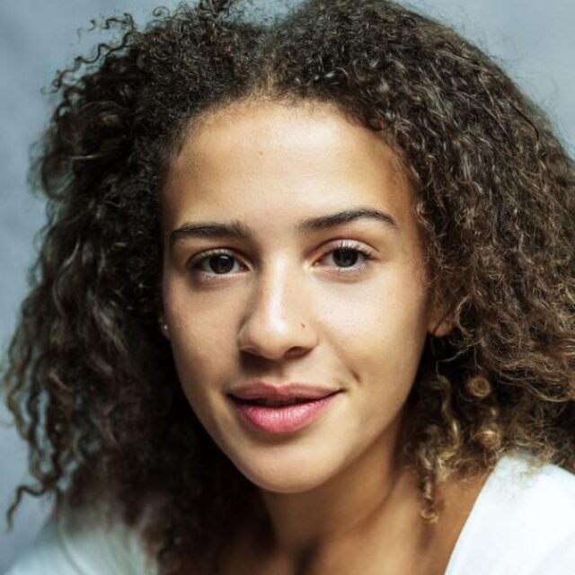 Close-up portrait of a young woman with curly hair, smiling gently at the camera