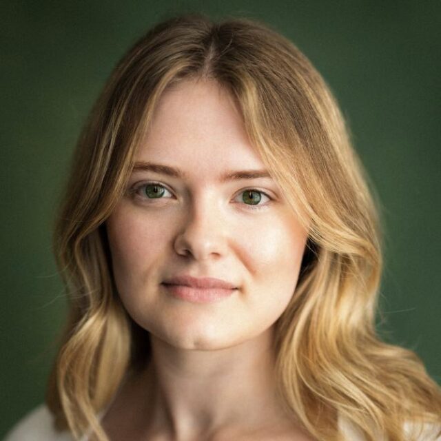 Close-up portrait of a young woman with wavy blonde hair and green eyes, against a green background