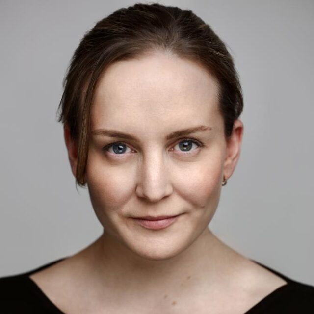 Headshot of a woman with brown hair pulled back, wearing a black top, smiling slightly at the camera