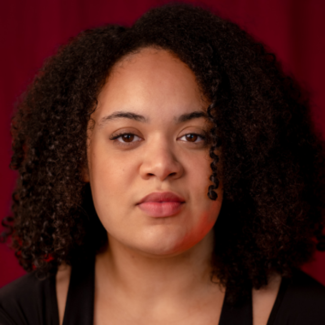 Woman with curly dark hair looking directly at the camera against a dark red background