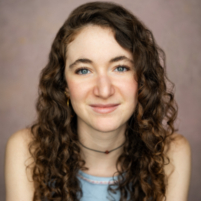 Woman with long curly brown hair and blue eyes, smiling in a portrait photo