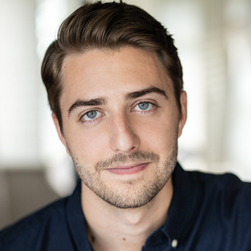 Headshot of a young man with short brown hair and light stubble, wearing a navy shirt