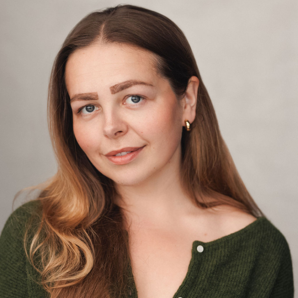 Portrait of a woman with long brown hair, wearing a green cardigan and gold earrings
