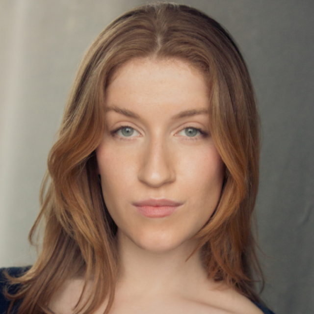 Headshot portrait of a woman with long reddish-brown hair, looking directly at the camera with a neutral expression
