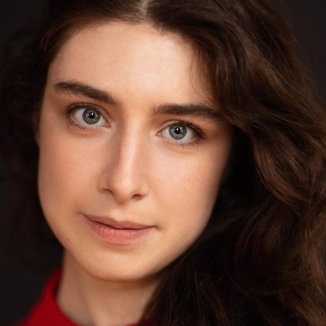 Close-up portrait of a woman with wavy dark hair and green eyes, wearing a red top