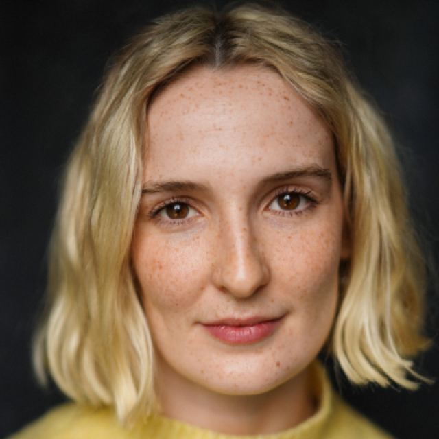 Close-up portrait of a woman with shoulder-length blonde hair and freckles, looking directly at the camera
