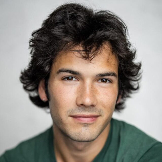 Portrait of a young man with curly dark hair, wearing a green top, looking directly at the camera