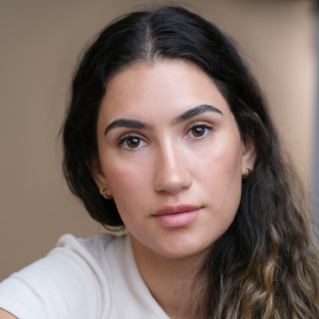 Close-up portrait of a young woman with long dark wavy hair, looking directly at the camera