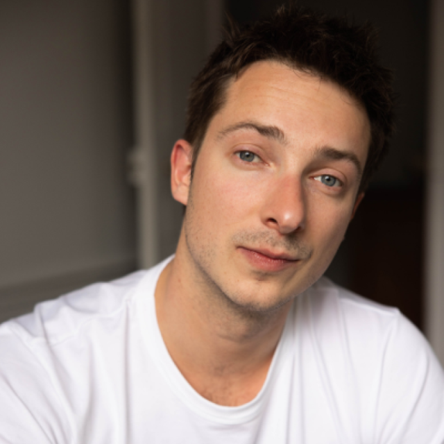 Young man with short brown hair wearing a white T-shirt, looking directly at the camera