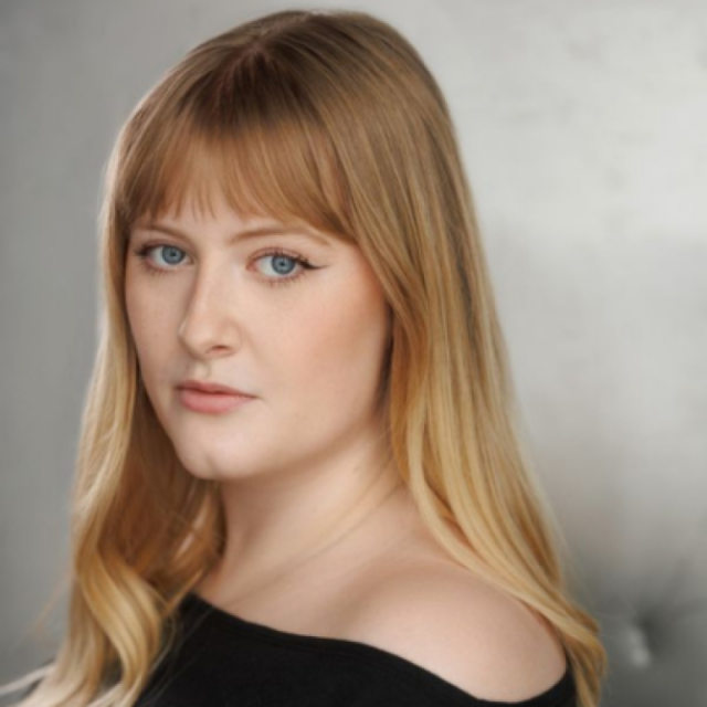 Portrait of a woman with long blonde hair and blue eyes, wearing an off-shoulder black top