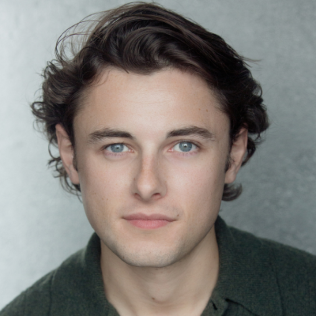 Headshot portrait of a young man with curly brown hair and blue eyes, wearing a dark green top