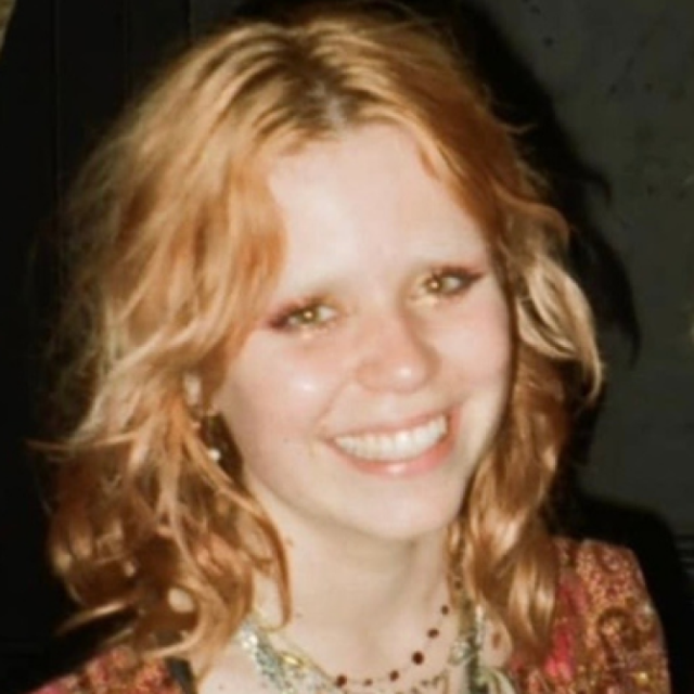 Young woman with curly reddish-blonde hair, smiling, wearing a patterned top and beaded necklace