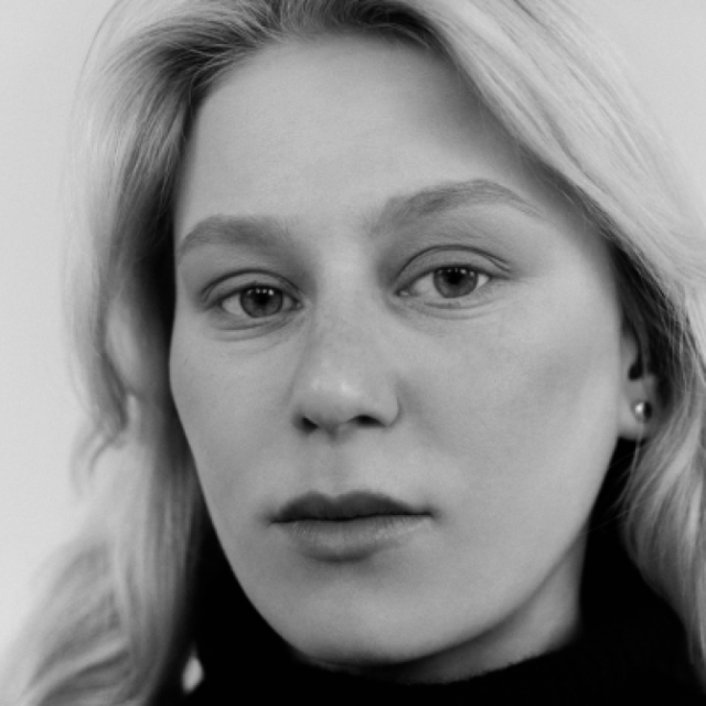 Black and white close-up portrait of a young woman with blonde hair, looking directly at the camera