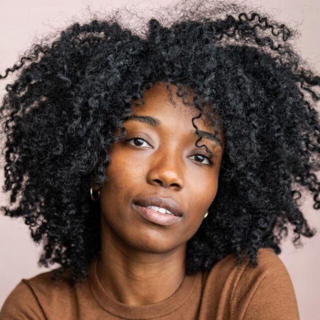 Woman with voluminous curly natural hair, looking directly at the camera with a relaxed expression