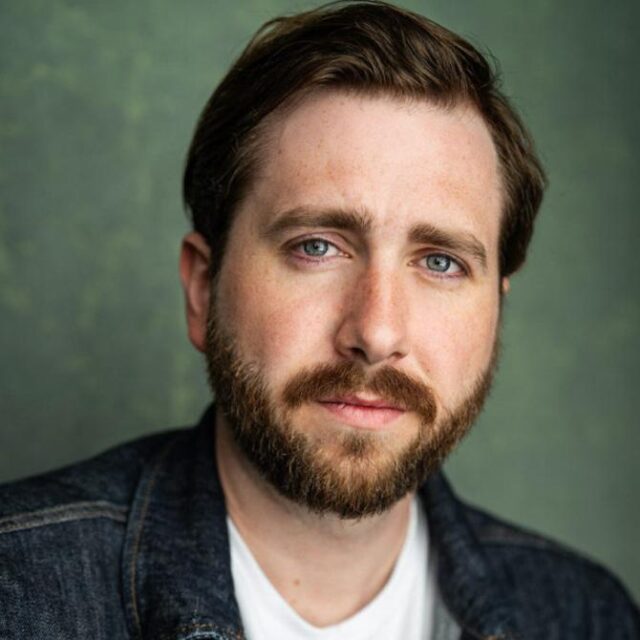 Portrait of a man with a beard, wearing a denim jacket over a white T-shirt, against a green background