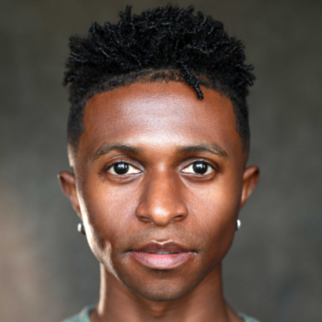 Close-up portrait of a man with short curly hair and stud earrings, looking directly at the camera