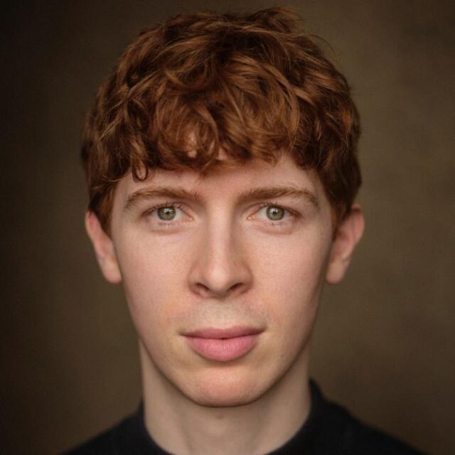Close-up portrait of a young man with curly ginger hair, looking directly at the camera