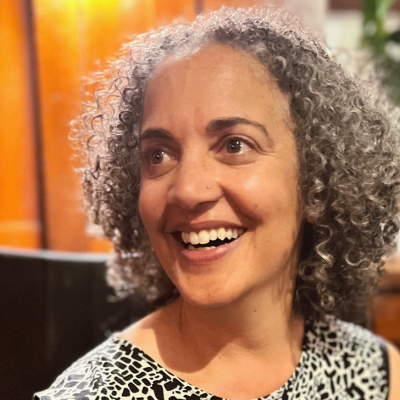 Woman with curly grey hair smiling, wearing a black and white patterned top