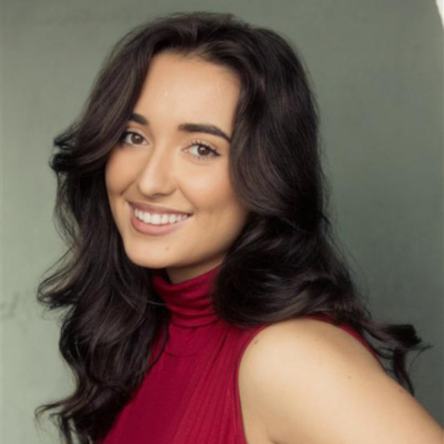Woman with long dark wavy hair smiling, wearing a red top, in a studio portrait