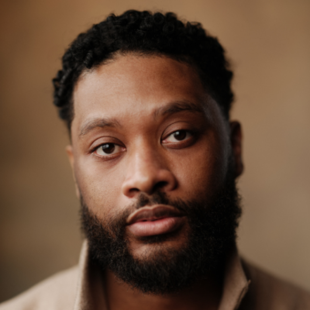 Close-up portrait of a man with a full beard and short curly hair, looking directly at the camera