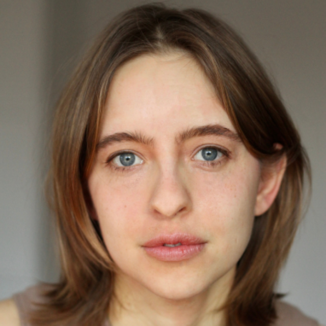 Close-up portrait of a young woman with brown hair and blue eyes, looking directly at the camera