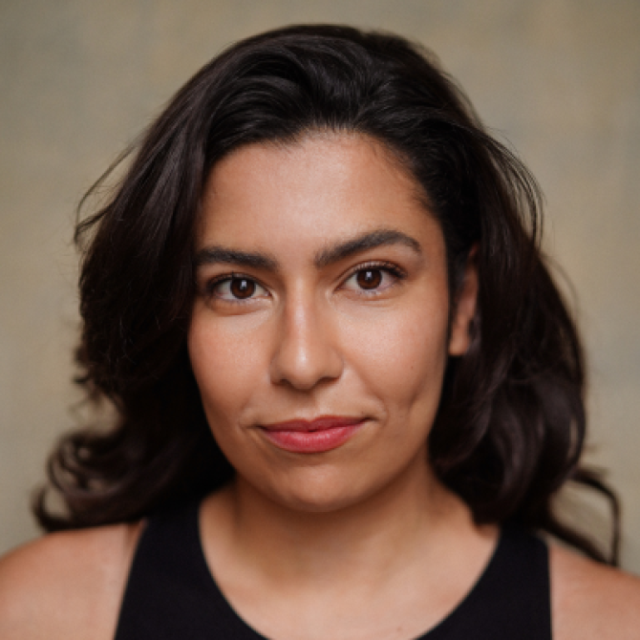 Portrait of a woman with long dark wavy hair, wearing a black top, looking directly at the camera